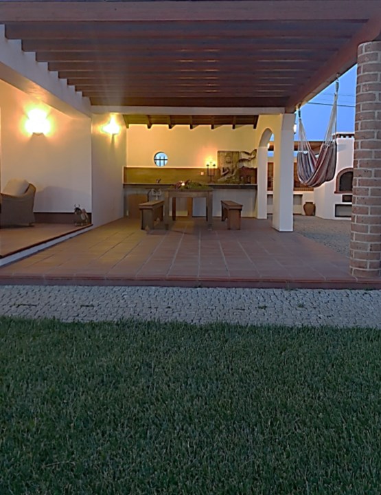 Alpendre coberto da Casa do Cortiço ao anoitecer, com mesa de refeições e candeeiros acesos